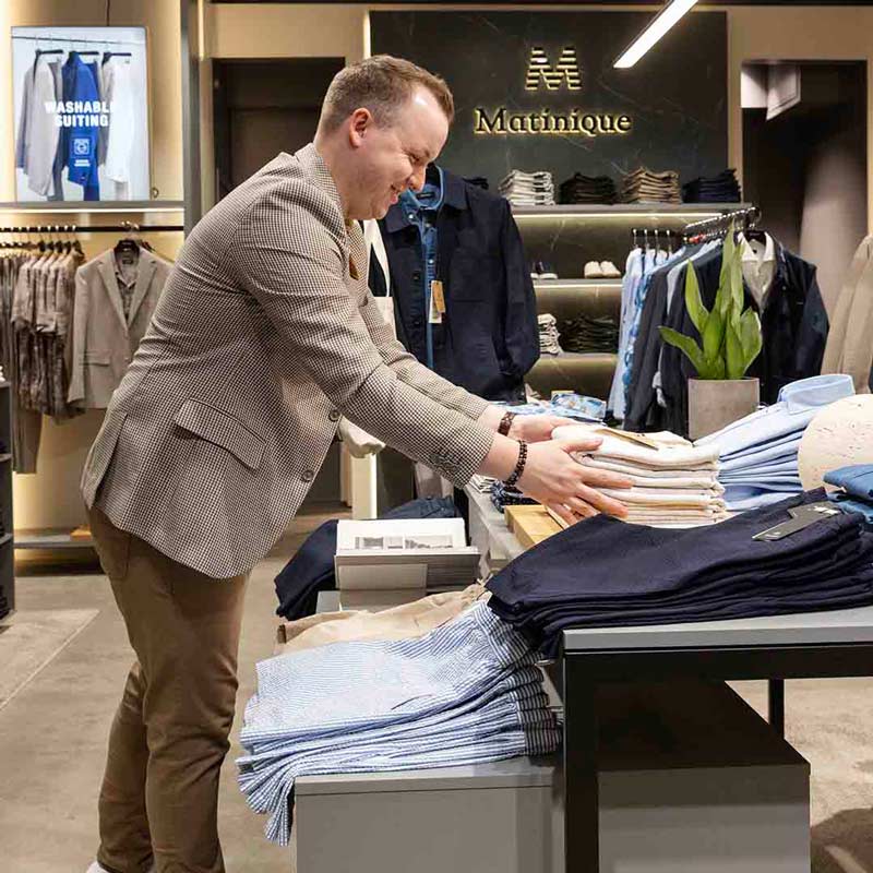 Employee from Matinique in Frederiksberg placing clothes on shelves.